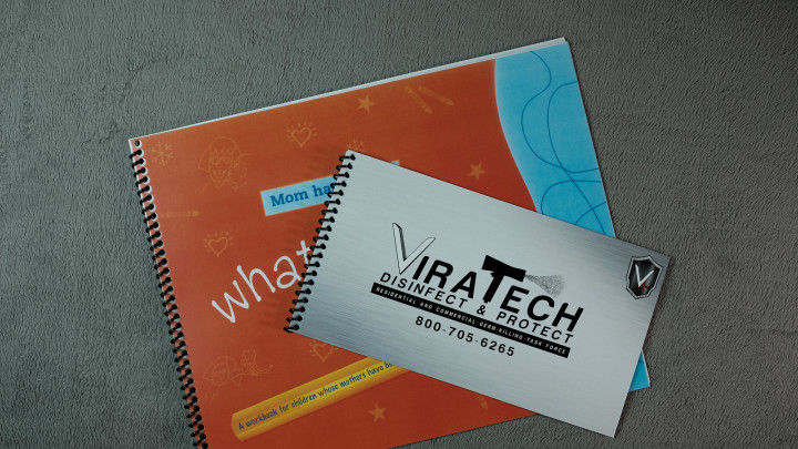 Spiral-bound book and business card. Book is orange and blue. Card is silver with company logo and phone number.