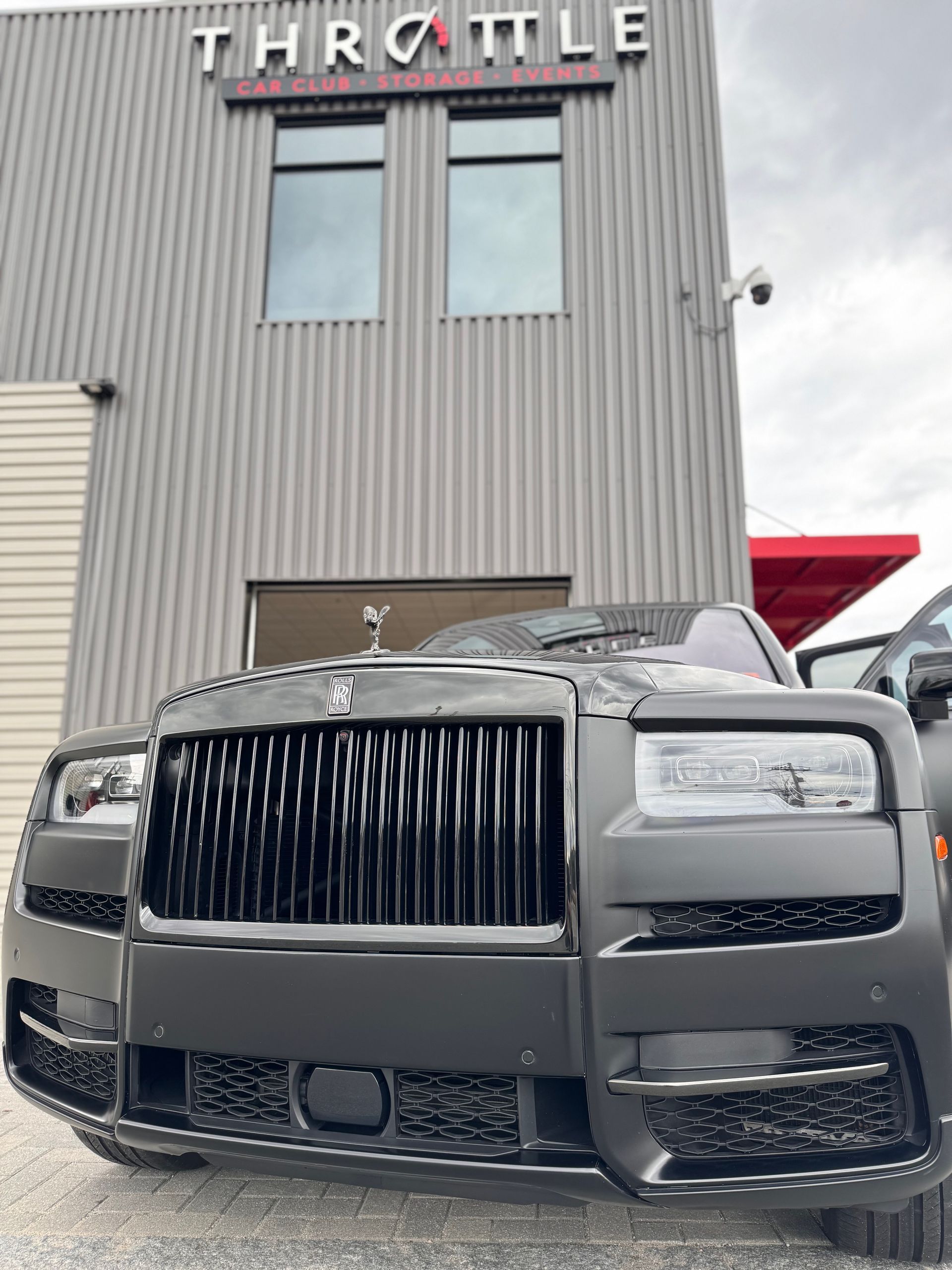 A black car is parked in front of a building that says throttle.