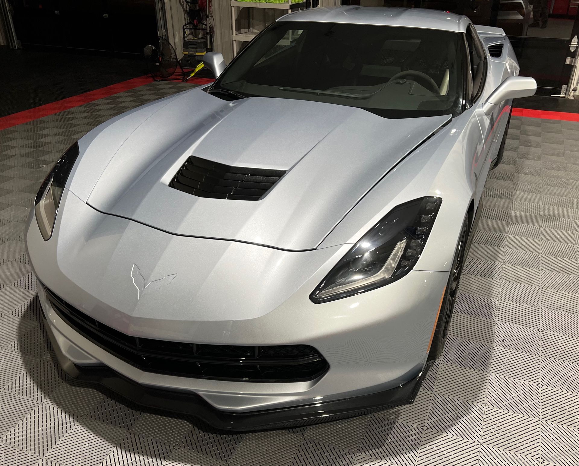 A silver corvette is parked on a tiled floor in a garage.