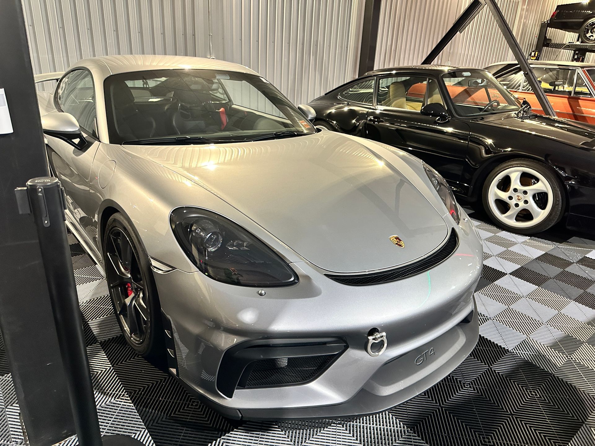 A silver porsche is parked in a garage next to a black car.