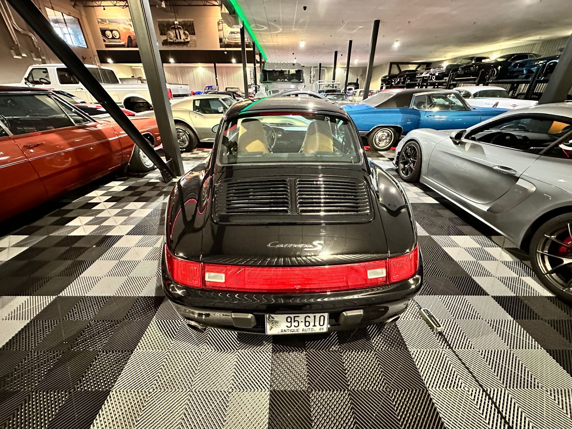 A black porsche 911 is parked in a showroom surrounded by other cars.