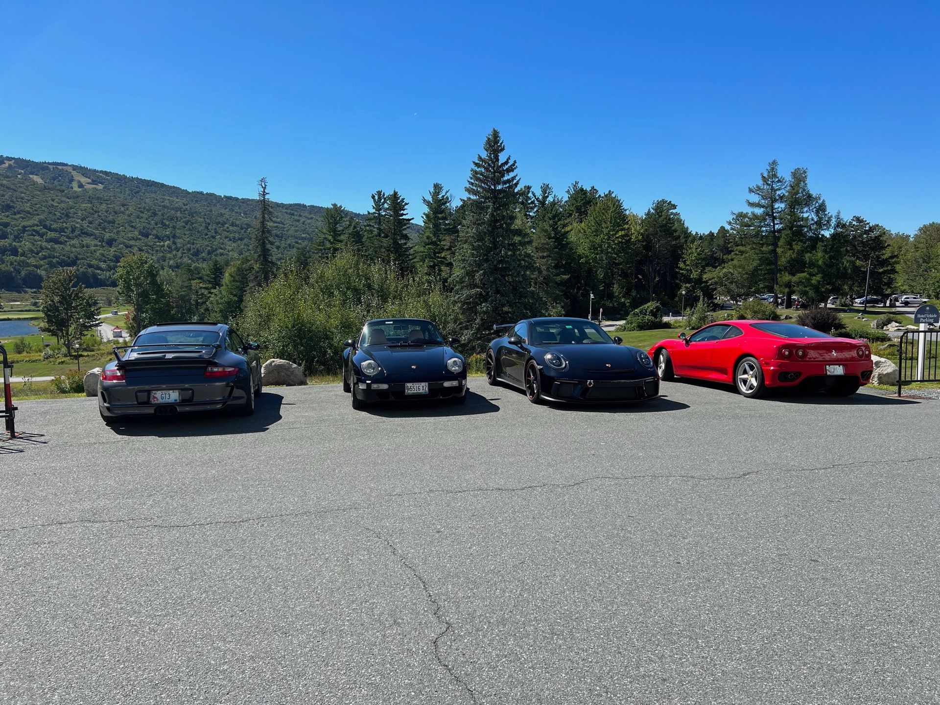Four sports cars are parked in a parking lot with trees in the background.