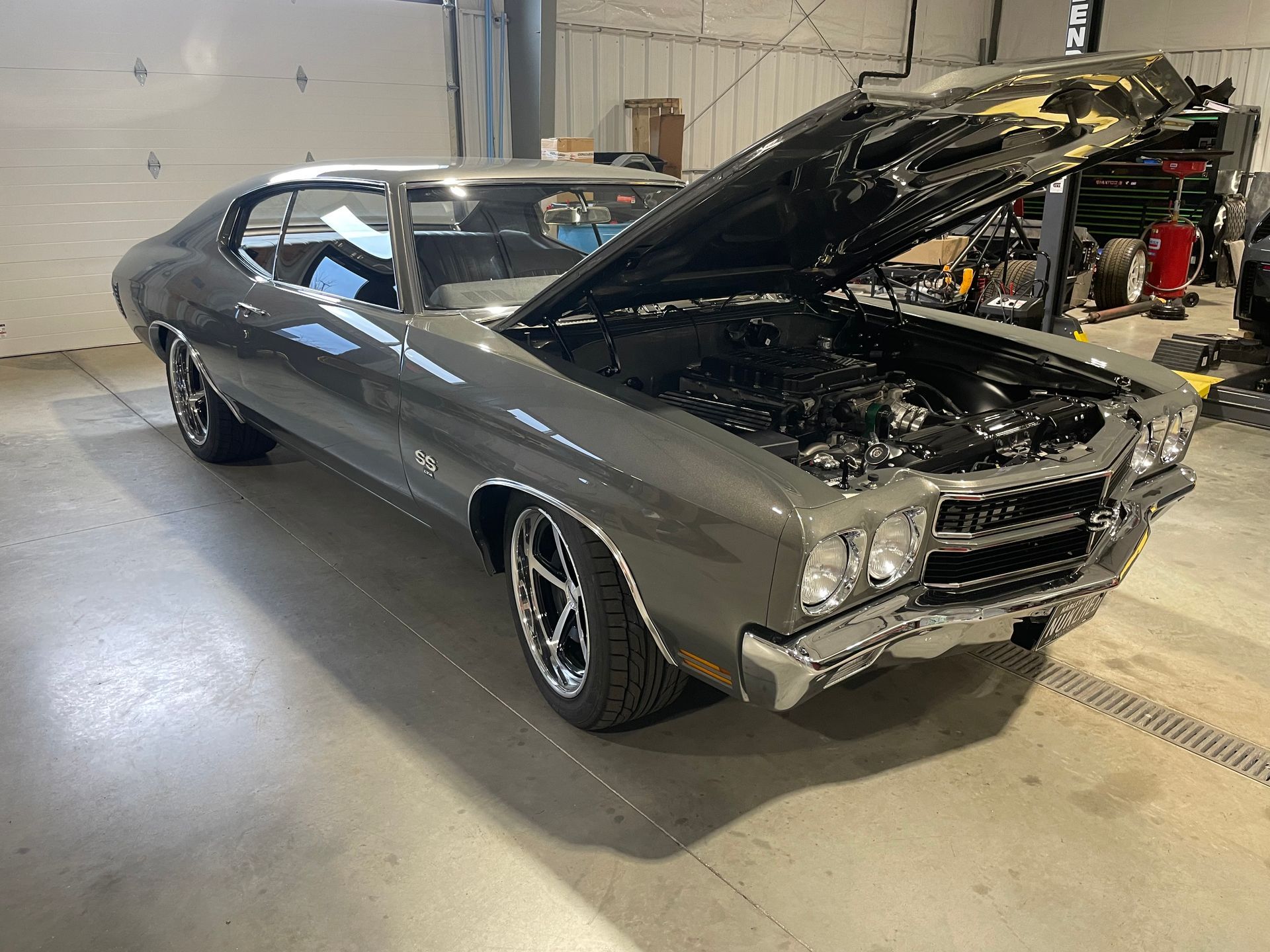 A gray car with the hood up is parked in a garage.