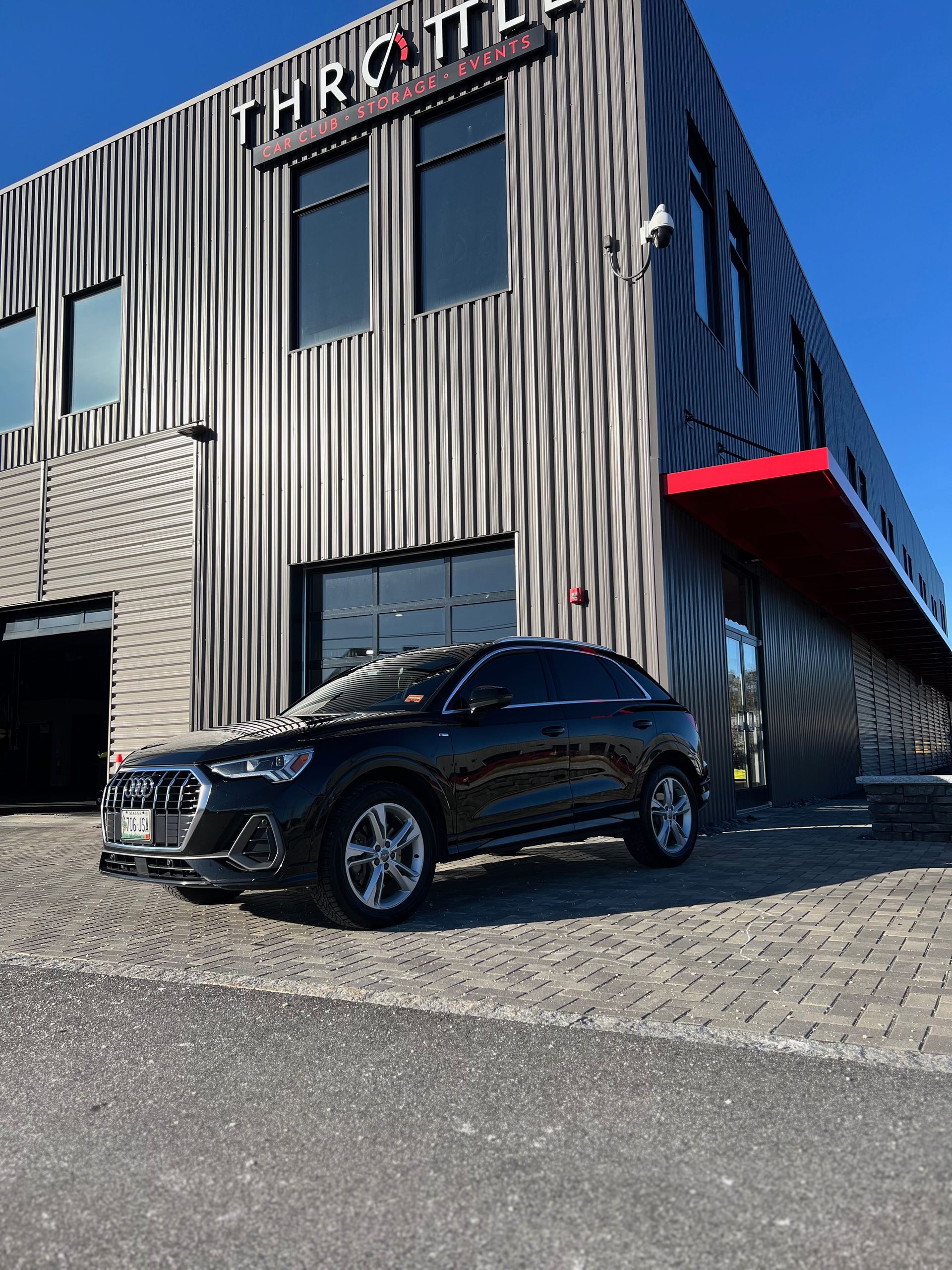 A black car is parked in front of a large building.