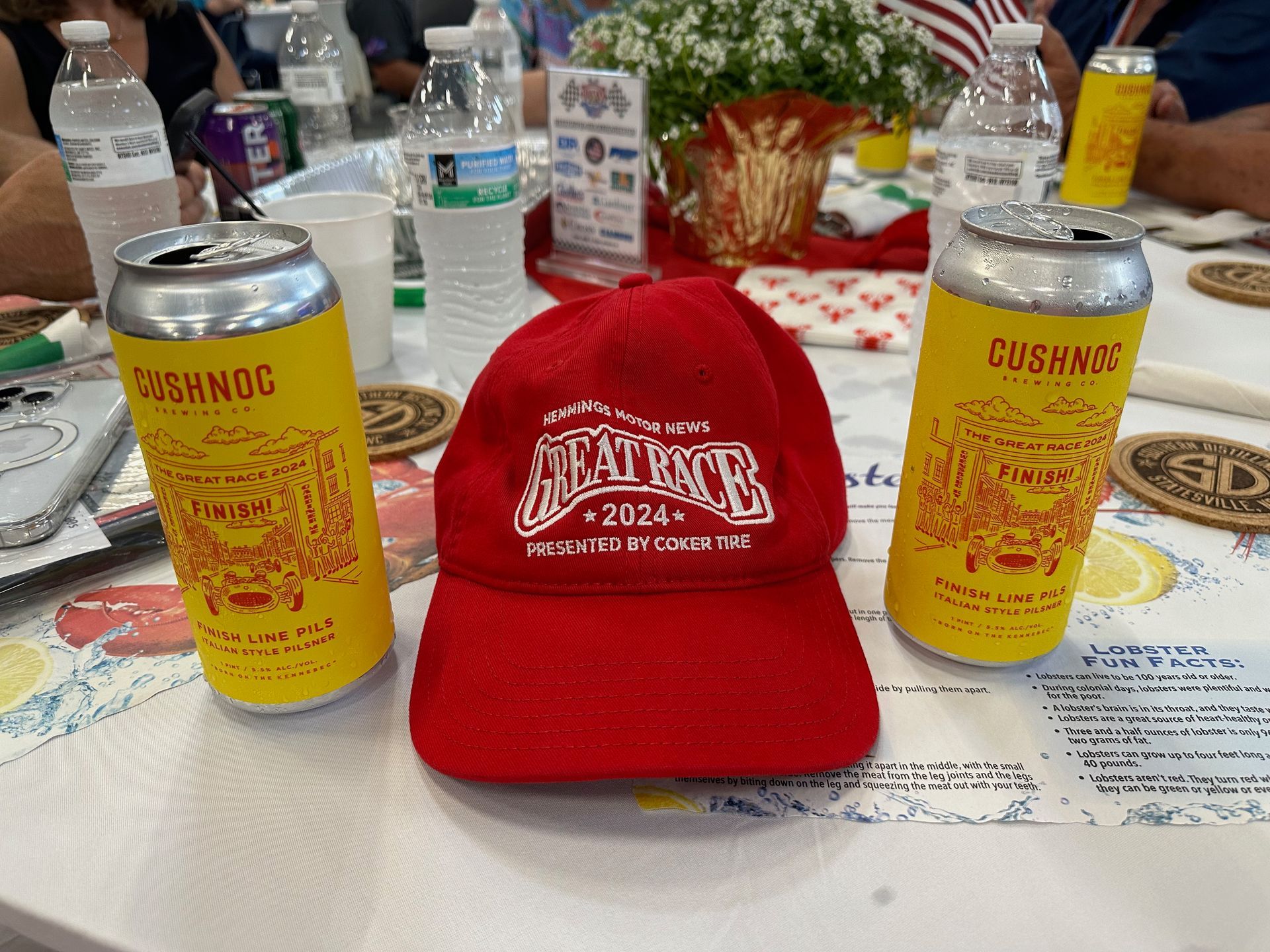A red hat is sitting on a table next to two cans of beer.