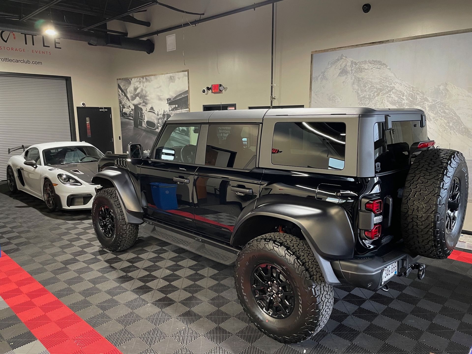 A black jeep is parked in a garage next to a white car.