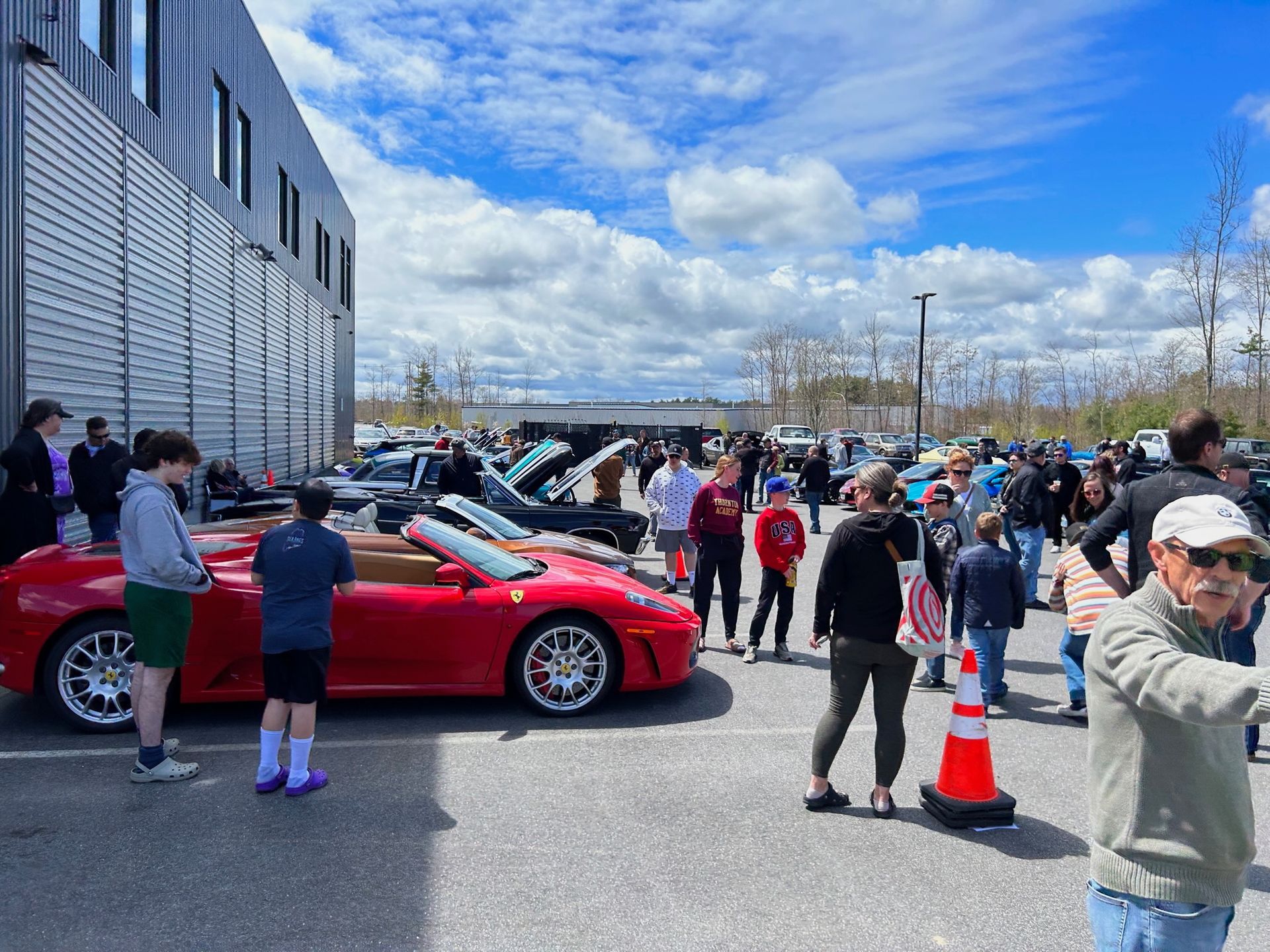 A group of people are standing around a red sports car in a parking lot.