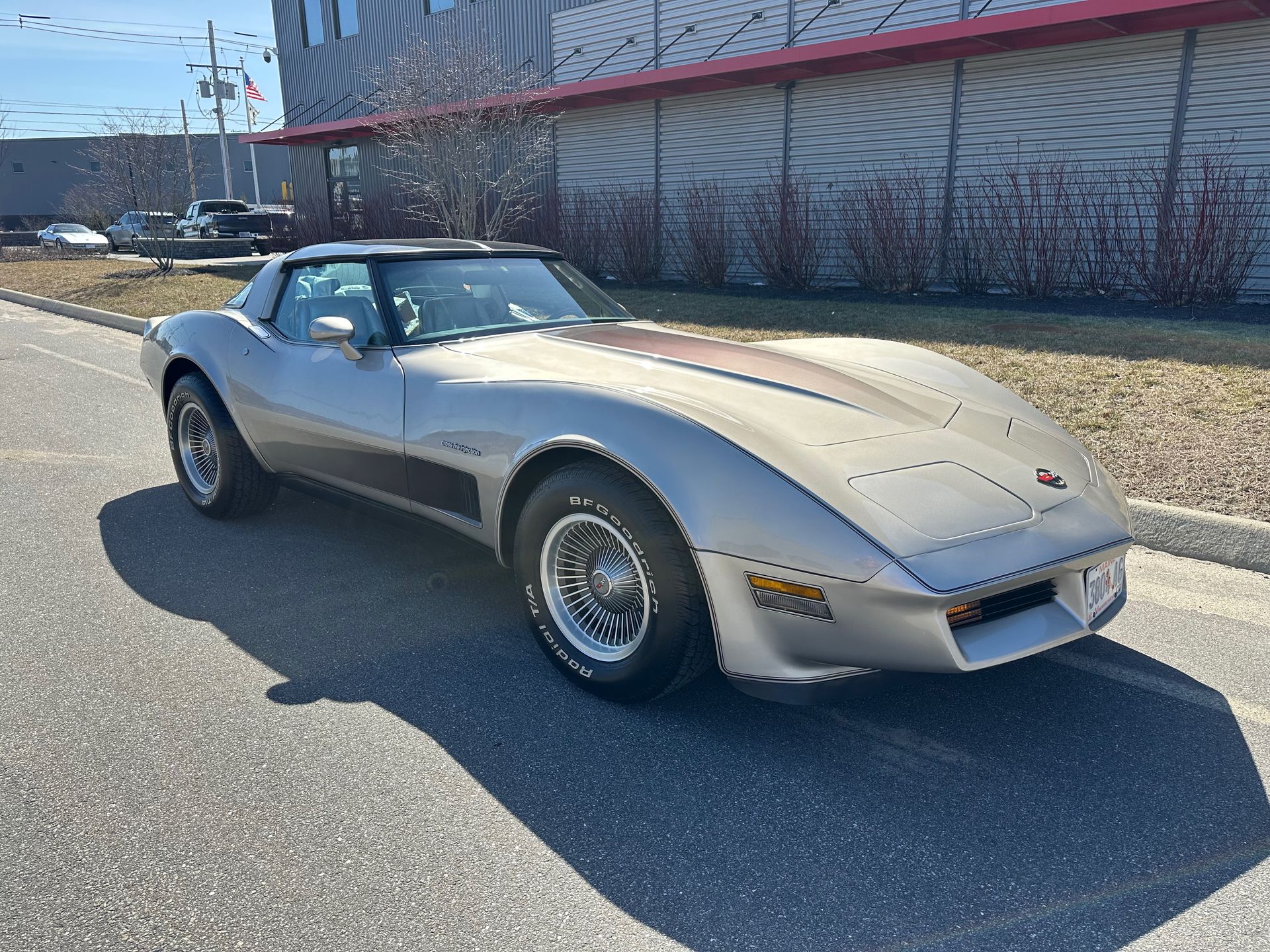 A silver corvette is parked on the side of the road in front of a building.