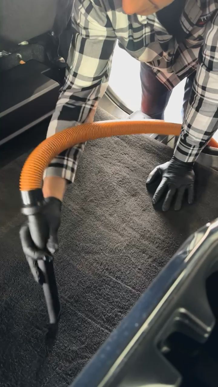 A person is using a vacuum cleaner to clean the carpet in a car.