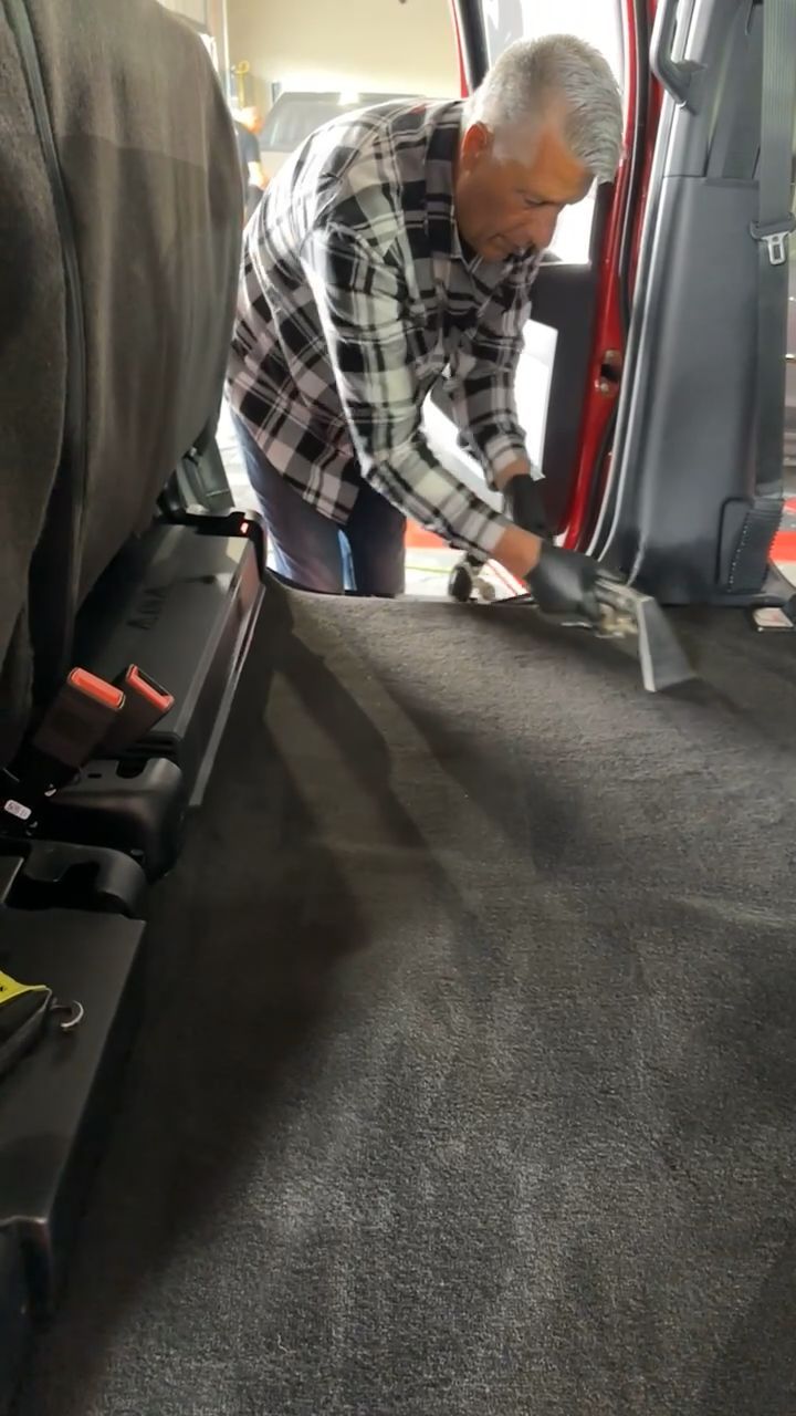 A man is cleaning the floor of a car with a vacuum cleaner.