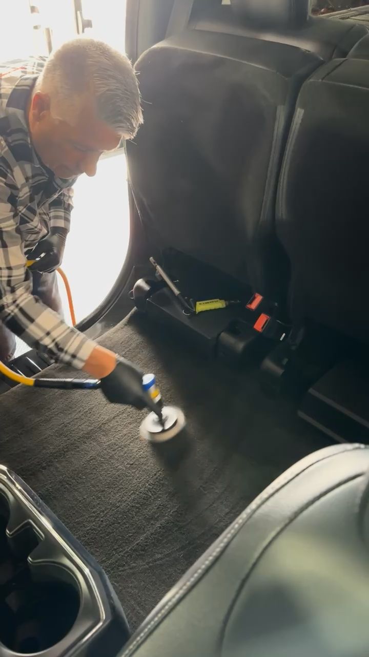 A man is cleaning the floor of a car with a vacuum cleaner.