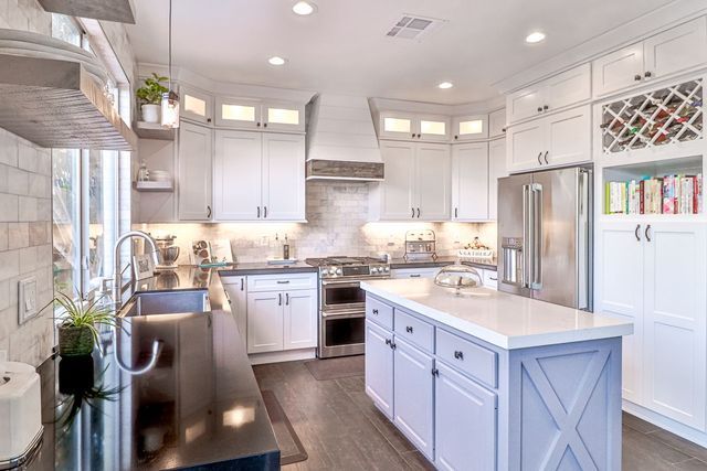 A kitchen with white cabinets , stainless steel appliances , and a large island.