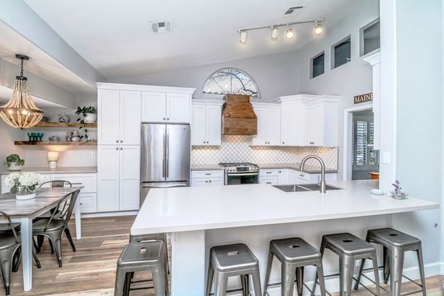 A kitchen with white cabinets , stainless steel appliances , a large island and stools.