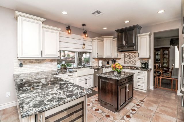 A kitchen with granite counter tops , white cabinets , and a large island.