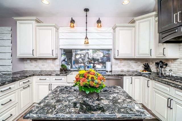 A kitchen with white cabinets , granite counter tops , and a large island with a vase of flowers on it.