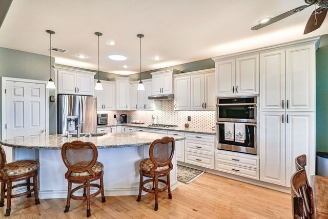 A kitchen with white cabinets , granite counter tops , stainless steel appliances and a large island.