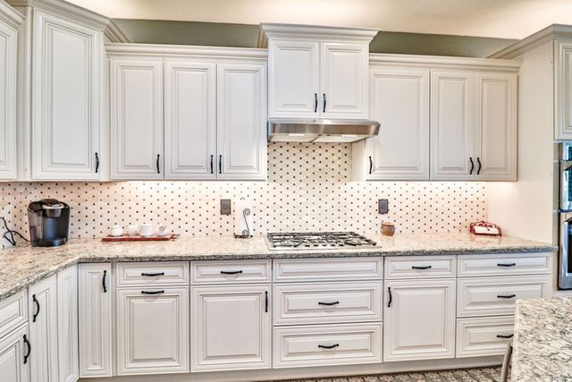 A kitchen with white cabinets , granite counter tops , and a stove top oven.