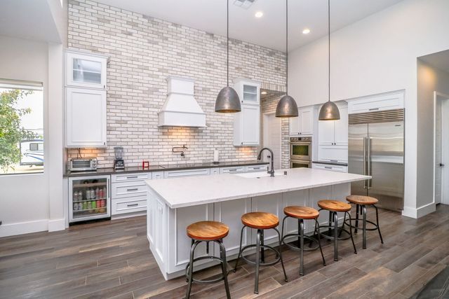 A kitchen with white cabinets , stools , a large island and a brick wall.