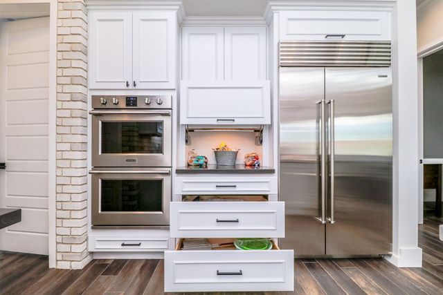 A kitchen with white cabinets and stainless steel appliances and drawers open.
