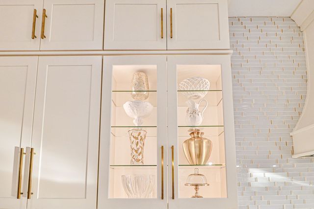 A kitchen with white cabinets and glass doors filled with vases and glasses.