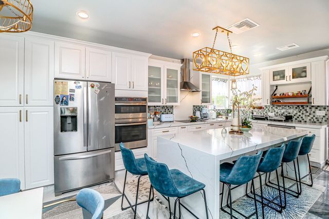 A kitchen with white cabinets , stainless steel appliances , a large island , and blue chairs.
