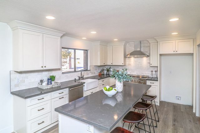 A kitchen with white cabinets , granite counter tops , stainless steel appliances and a large island.