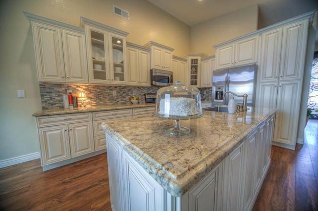 A kitchen with white cabinets , granite counter tops , stainless steel appliances and a large island.