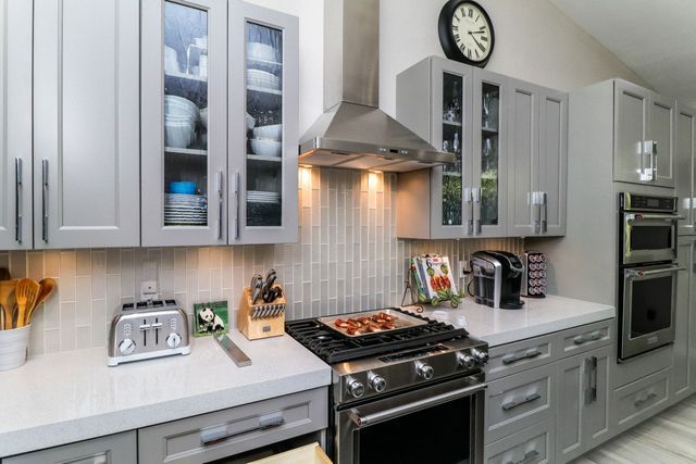 A kitchen with gray cabinets , stainless steel appliances and a clock on the wall.