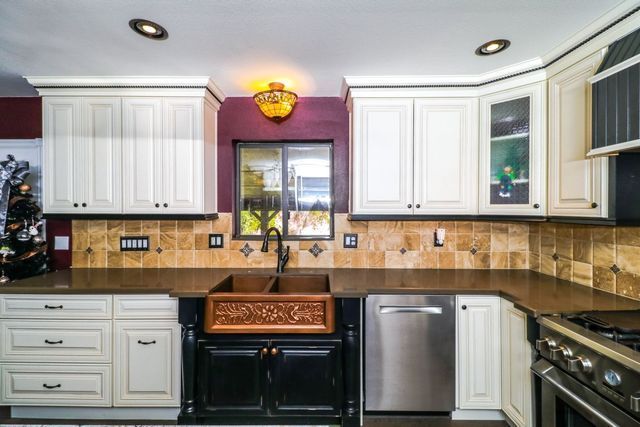 A kitchen with white cabinets , stainless steel appliances , a sink and a window.