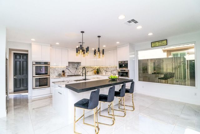 A kitchen with white cabinets , black counter tops , gold stools and a large island.