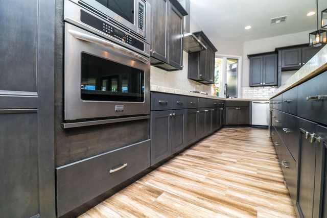 A kitchen with gray cabinets , stainless steel appliances , and hardwood floors.