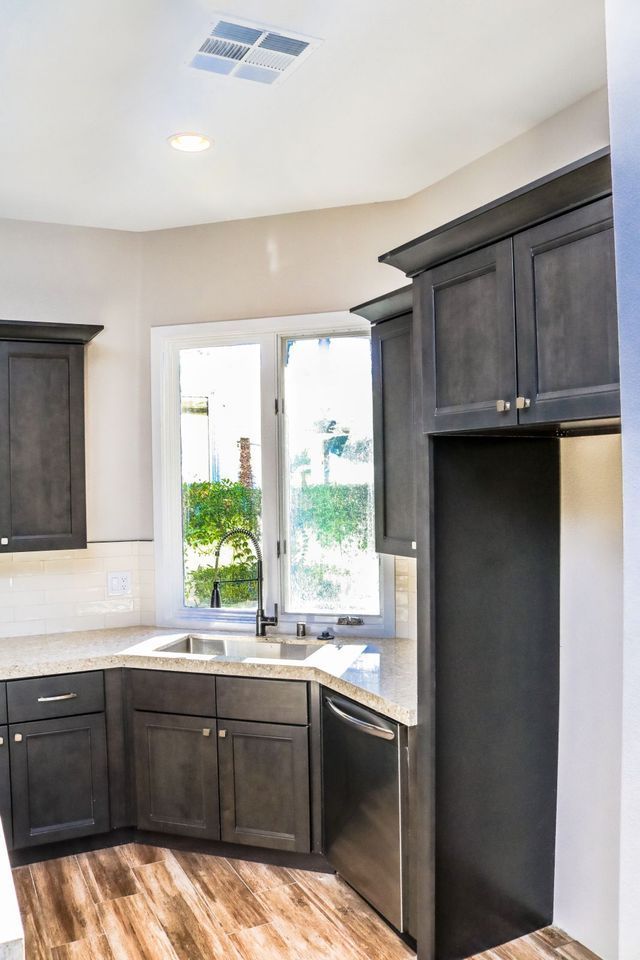 A kitchen with black cabinets , stainless steel appliances , a sink , and a window.