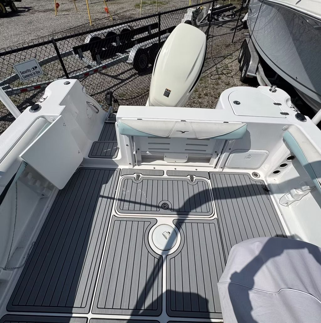 Gray and white boat deck with cushioned seating and an outboard motor.