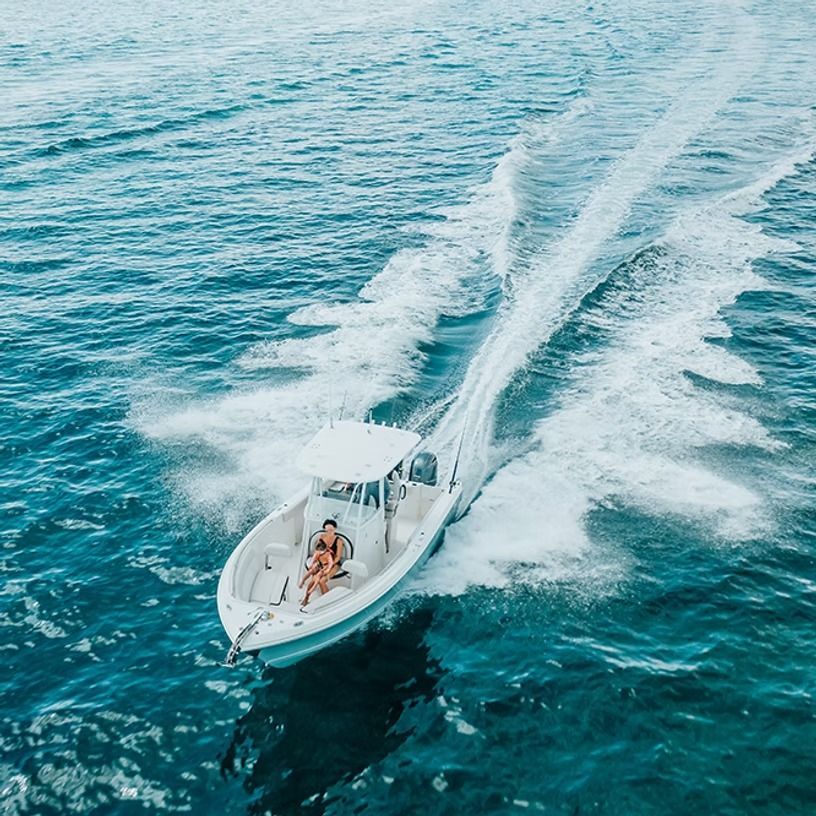 White motorboat speeding across blue ocean; two people onboard enjoying the ride.