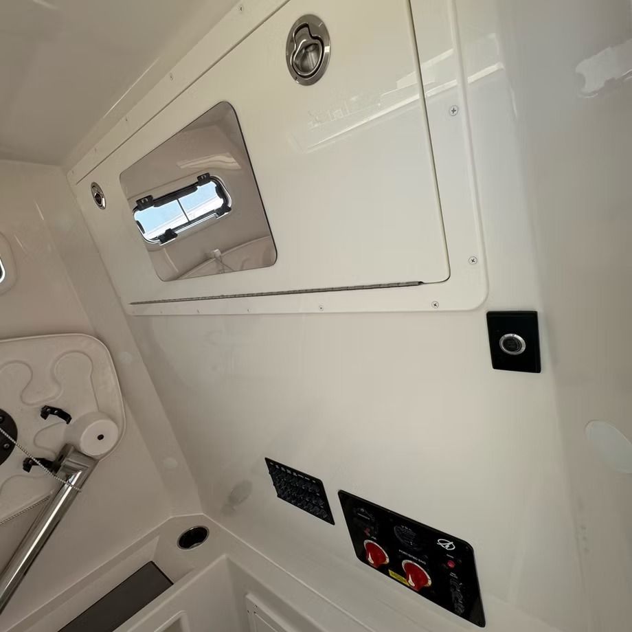 Interior of a boat cabin, white walls, a storage compartment, control panel, and a small window.