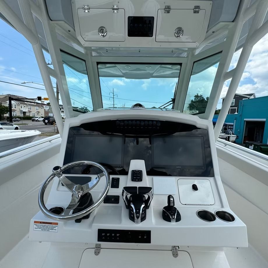 Boat dashboard with steering wheel, navigation screens, and controls. Bright, sunny day.
