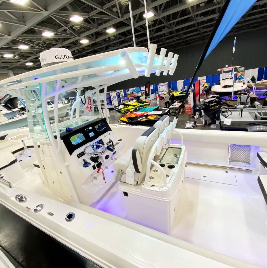 White boat at a boat show, with control panel, radar, and seating. Other boats and people in the background.