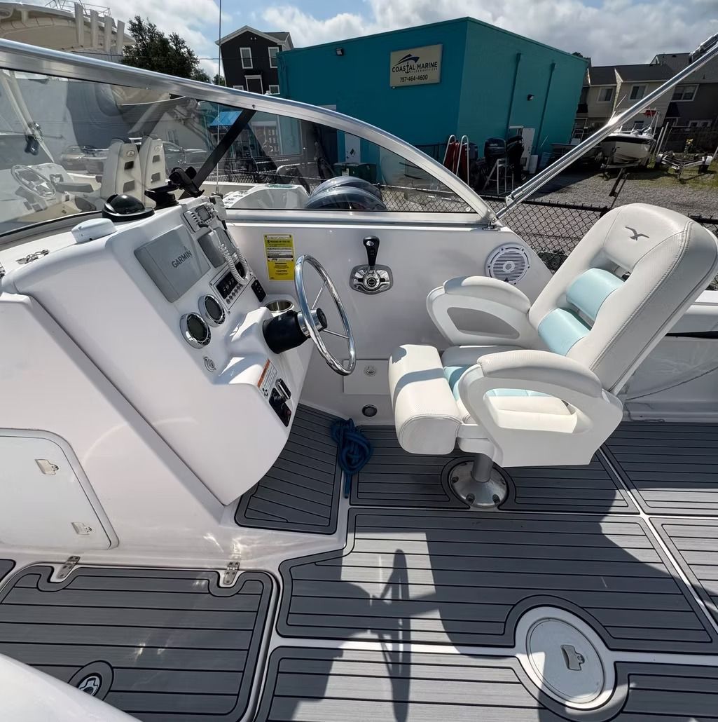 Boat interior with white captain's chair, steering wheel, gauges, and gray flooring. Blue building in background.