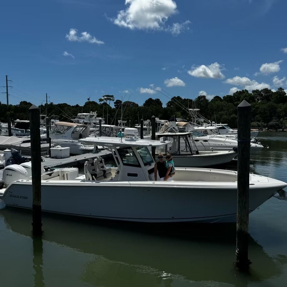 Boats docked at a marina on a sunny day; two people are on a white boat.