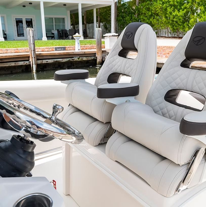 Two white boat seats with black armrests and headrests. Steering wheel visible. Outdoors by water.