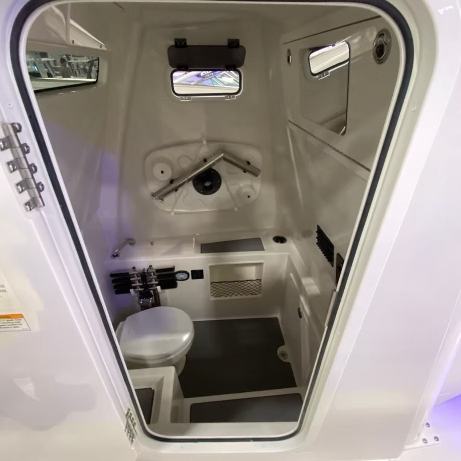 Interior of a white boat head (bathroom) with a toilet, sink, and small window.