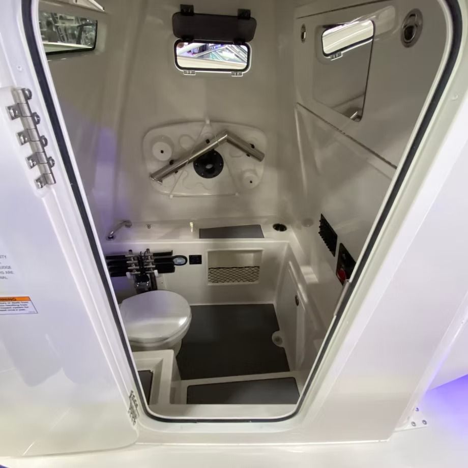 Inside a boat's enclosed head (bathroom). White walls, toilet, sink area, overhead storage.