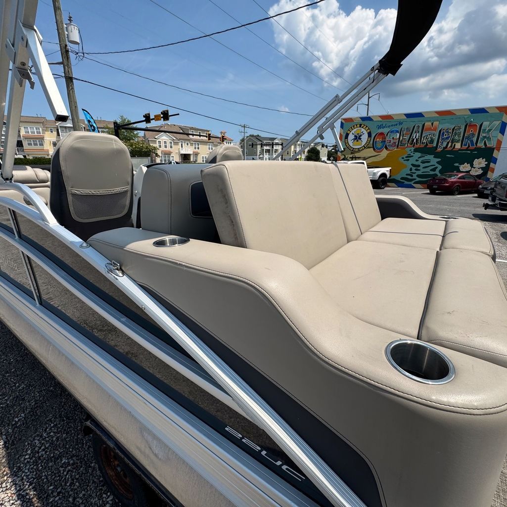 Pontoon boat with beige seating and cup holders, outdoors under a blue sky.