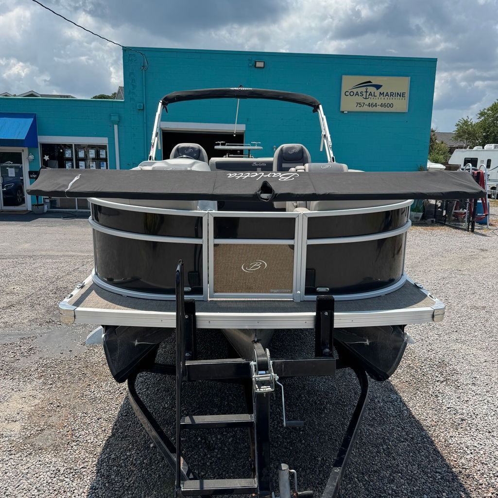 Black pontoon boat on trailer in front of a blue building with a sign.