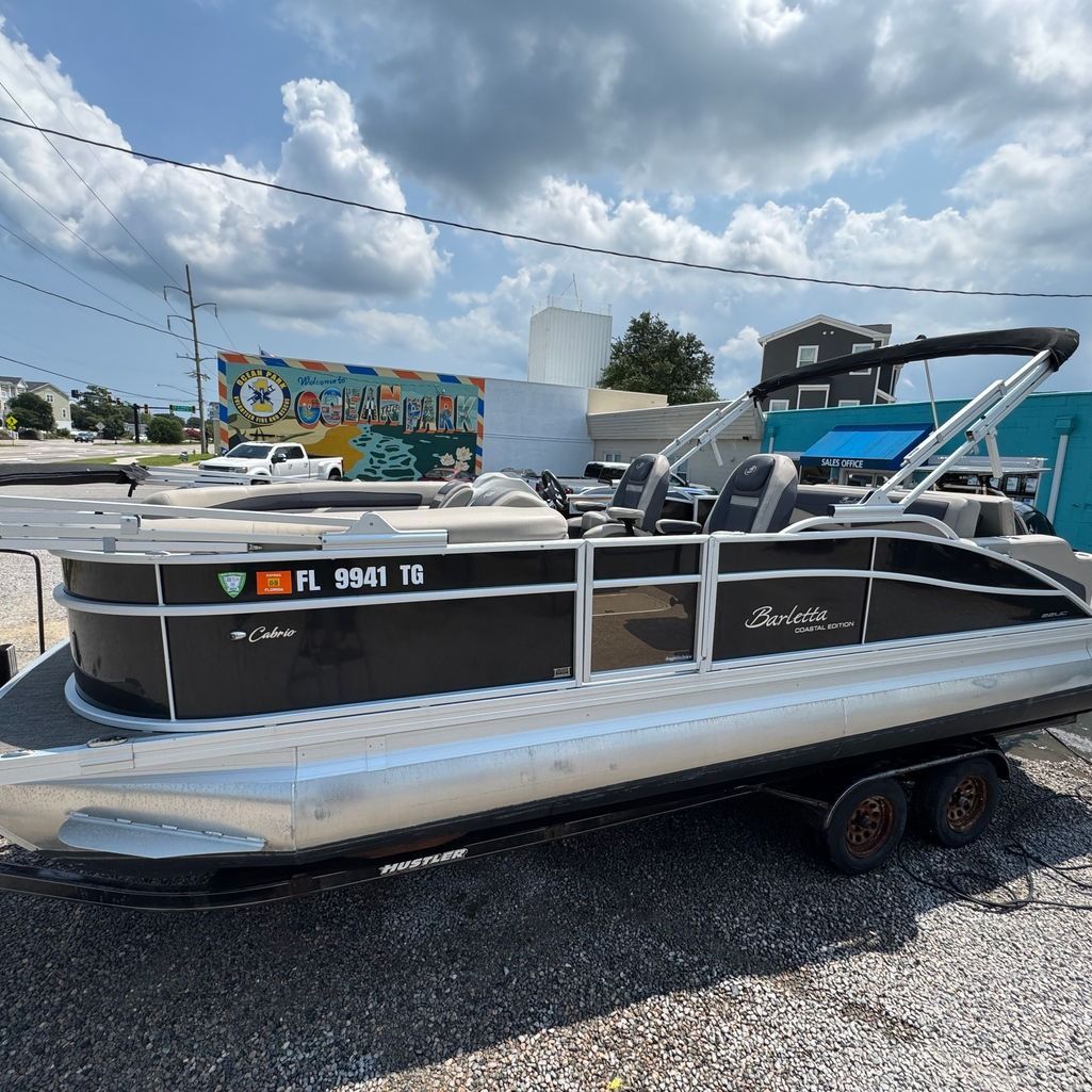 Black and silver pontoon boat on a trailer, outdoors on a sunny day.