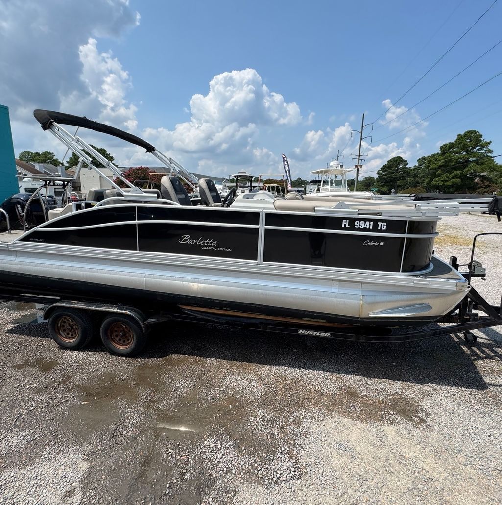 Black and silver pontoon boat on a trailer in an outdoor lot, sunny day.