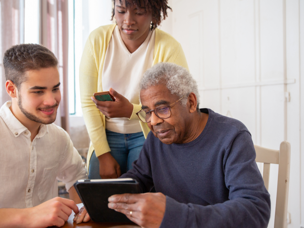 An elderly couple is sitting at a table using a laptop computer.