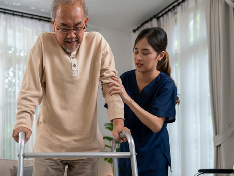 A nurse is helping an elderly man walk with a walker.