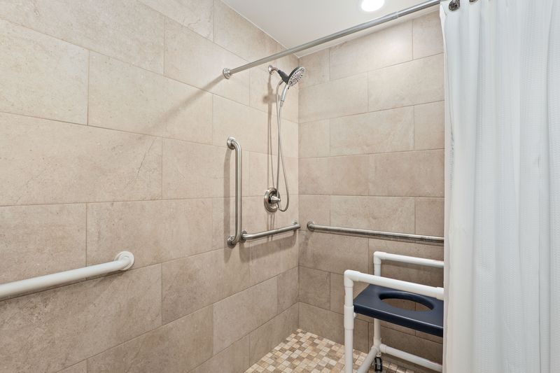 A bathroom with a shower , a toilet , and a stool.