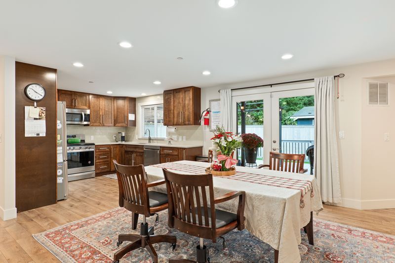A dining room with a table and chairs and a kitchen in the background.
